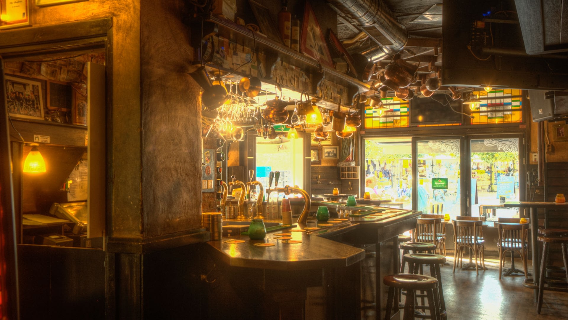 Interieur van bruine kroeg De Slimmerick in Naaldwijk met een bruine bar, barkrukken , zacht licht en hangende glazen boven de bar