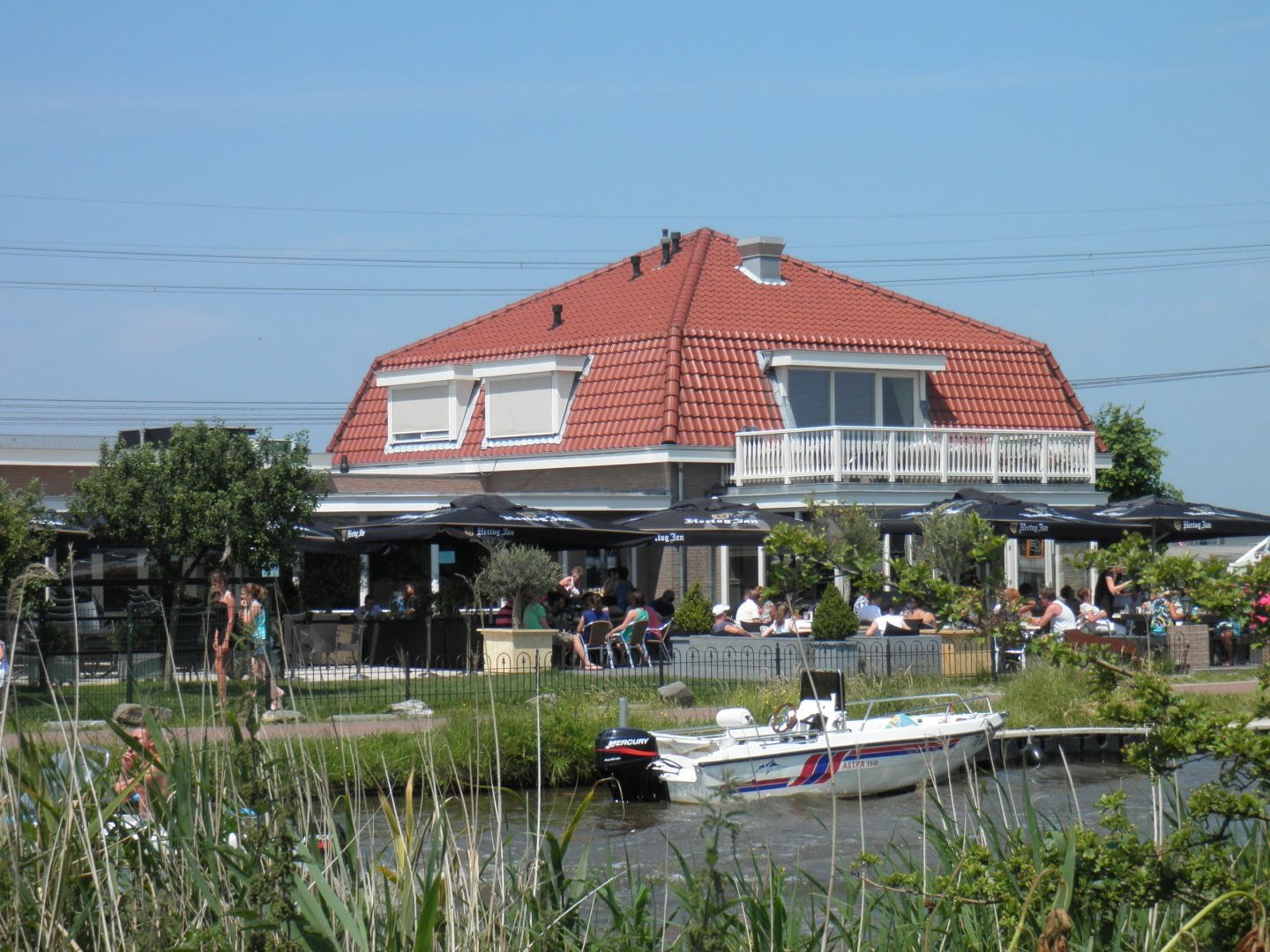 uitzicht over het water op het pand en terras van eetcafé de Bonte Haas met bootjes voor de deur in het Westland
