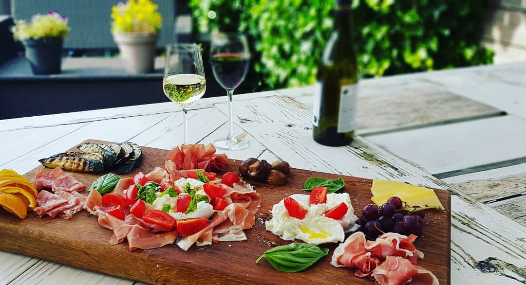 houten plank met Italiaanse anti-pasta gerechten op een witte houten tafel met twee glazen wijn en een fles wijn in de achtergrond bij Poveretti in het Westland