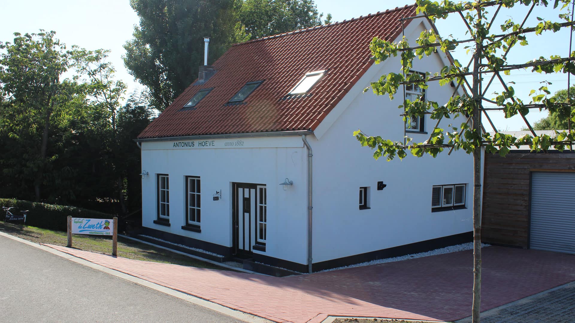 Vrijstaand wit vakantiehuisje met rood dak met de naam Antonius Hoeve onderaan de dijk bij Paviljoen de Zweth in het Westland