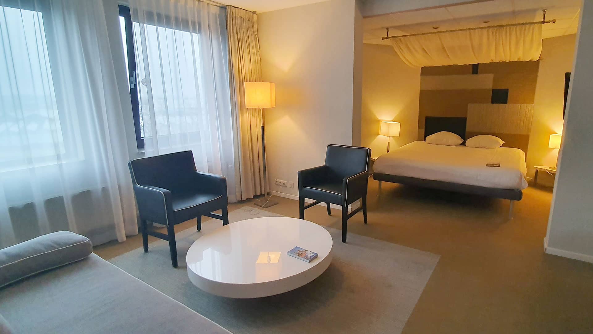 ruime hotelkamer in Fletcher Hotel Restaurant Carlton in het Westland met een hemelbed en een zithoek met losse stoelen en een grijze bank