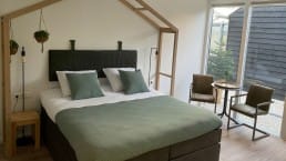 Tweepersoons bed in een B&B met groen/grijze dekbed en een houten frame van een kas boven het bed in het Westland