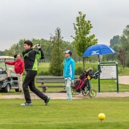 jonge speler slaat af op de tee van Golfbaan Delfland tijdens een jeugdtournooi en een andere speler en wedstrijdofficial kijken toe in het Westland
