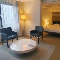 ruime hotelkamer in Fletcher Hotel Restaurant Carlton in het Westland met een hemelbed en een zithoek met losse stoelen en een grijze bank