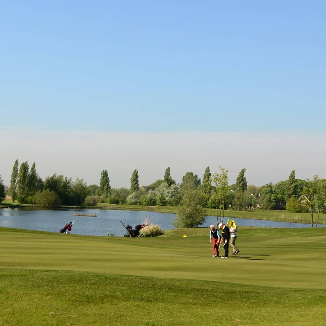 Spelers lopen in de golfbaan van Golfbaan Delfland in het Westland met voor zich de green en rechts een grote watervlakte