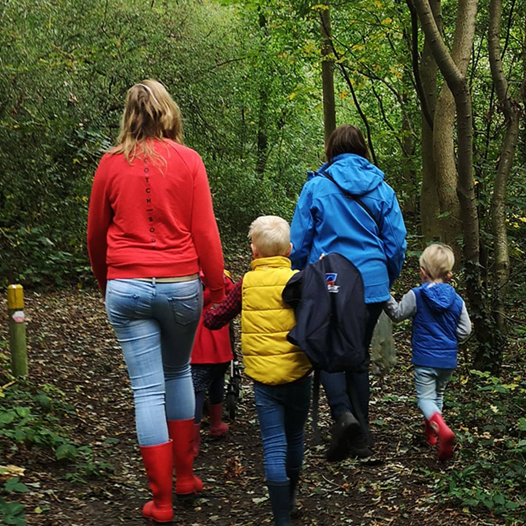 Familie met twee volwassenen en drie kinderen lopen door het Staelduinse Bos in het Westland met felgekleurde jassen aan