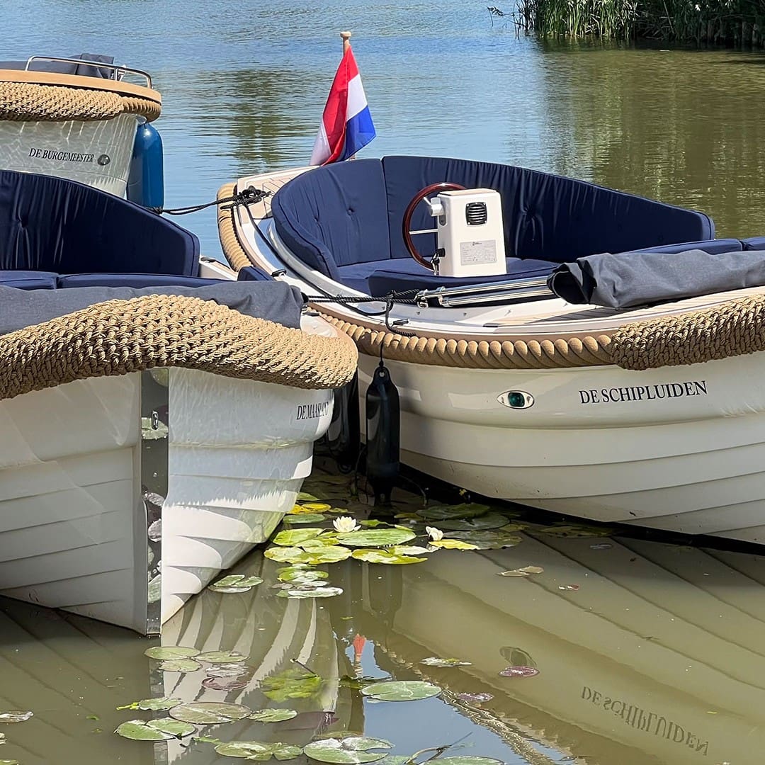 luxe elektrische sloepen van Floriette Experience en 1 motorsloep in het water met witte scheepsromp en blauwe kussens op een zonnige dag in Schipluiden voor een vaartocht naar het Westland