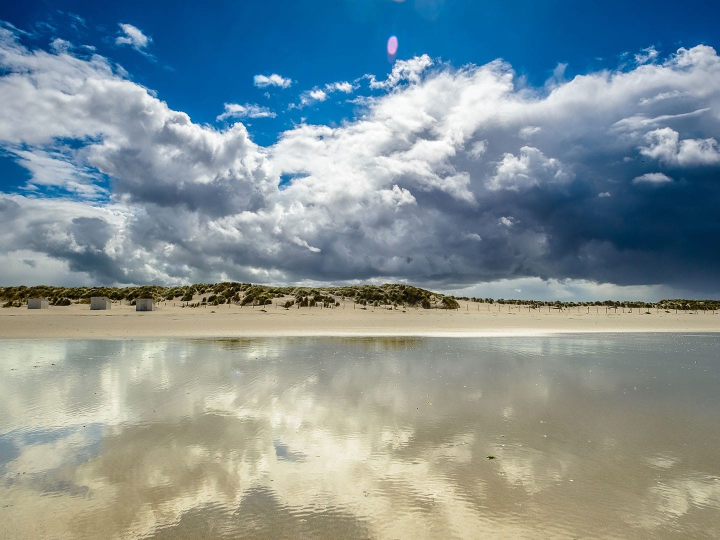 foto vanuit de zee richten de kust en duinen van het westland met een leeg strand, witte houten huisjes op het strand en grote witte wolken boven land