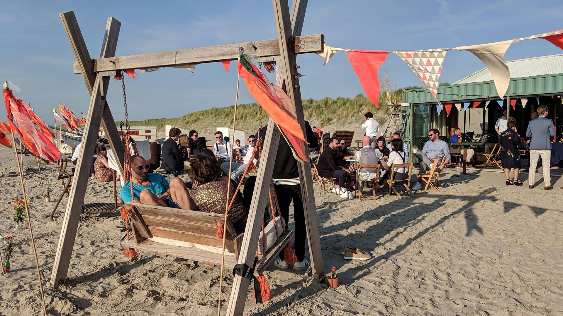 houten schommel op het strand bij Strandtent De Pit inn het Westland op een zonnige dag met in de achtergrond mensen die genieten van een feestje aan het strand