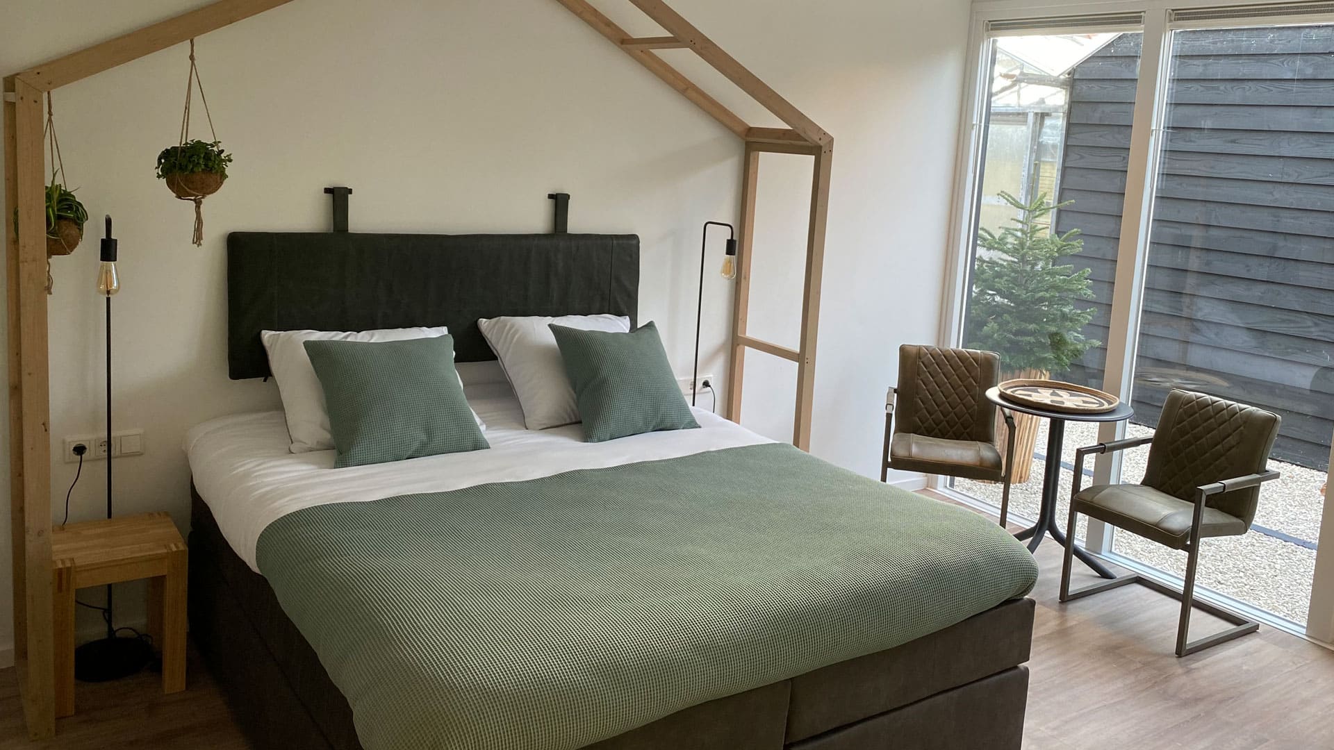 Tweepersoons bed in een B&B met groen/grijze dekbed en een houten frame van een kas boven het bed in het Westland