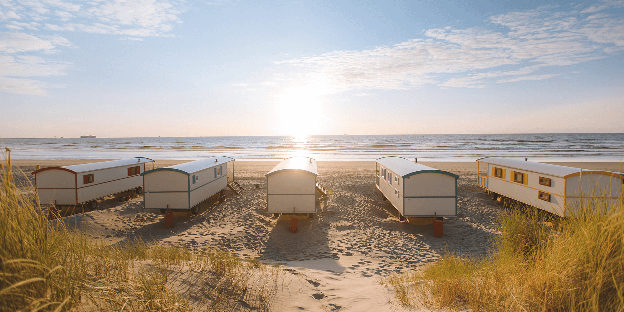 5 pipowagens op het strand van het Westland met duinen op de voorgrond en de zee in de achtergrond