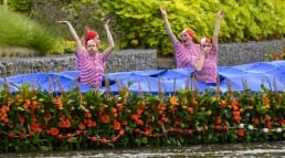 in rood-wit gestreepte t-shirts verklede dames dansen aan boord van een met bloemen versierde boot tijdens het Varend Corso in het Westland