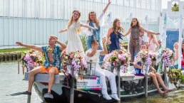 in zomerse jurkjes verklede dansgroep op een met bloemen versierde boot tijdens het Varend Corso in het Westland