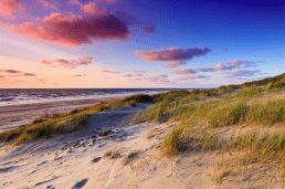 foto van zandduinen in het Westland begroeid met groen helmgras en in de achtergrond de zee met wolken en een rode gloed van de zon