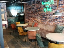 entree van restaurant Eindeloos in het Westland met een lange leren bank langs de muur en kleurrijke leren stoeltjes en witte tafels en een neontekst aan de muur in het Westland