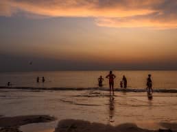 families die op het strand van het Westland aan het zwemmen zijn in zee nadat de zon is ondergegaan aan de kust