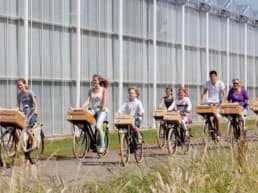 Famile van zeven personen fietst op een warme zomerse dag langs een wit gespoten kas in het Westland
