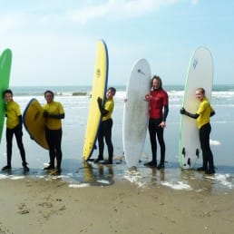 familieleden staan in wetsuits op het strand met grote surfplanken in hun handen tijdens een surfles op zee van Dreams in het Westland