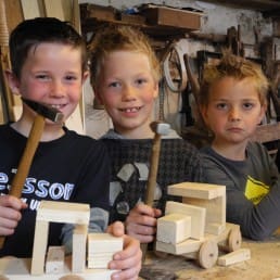 drie jonge jongetjes die dehouten autootjes laten zien die ze gemaakt hebben tijdens een workshop bij Museum de Timmerwerf in het Westland