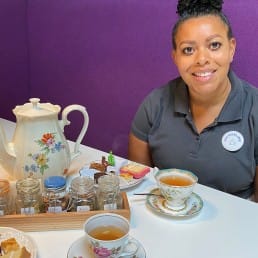medewerker Jacqueline van Lunchroom Bijzonder zit aan tafel in de lunchroom met een high tea met verschillende soorten verse thee en een schaal met zoetigheden in het Westland