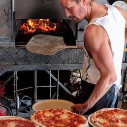 eigenaar Mathijs bakt de bekende pizza's van Strandtent De Pit in een brandende pizzaoven op het strand in het Westland