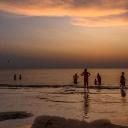 families die op het strand van het Westland aan het zwemmen zijn in zee nadat de zon is ondergegaan aan de kust
