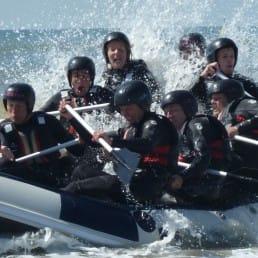 Groep volwassenen varen in een rubberen raftboot in de branding van de zee met opspattend water in het Westland