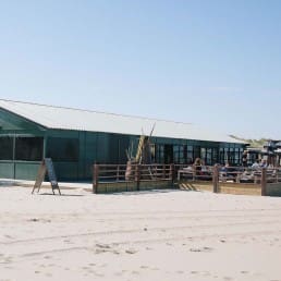 buitenzijde van strandtent Bondi Beach Club op het strand in Monster in het Westland met een groene houtel gevel en dank en een terras in de zon